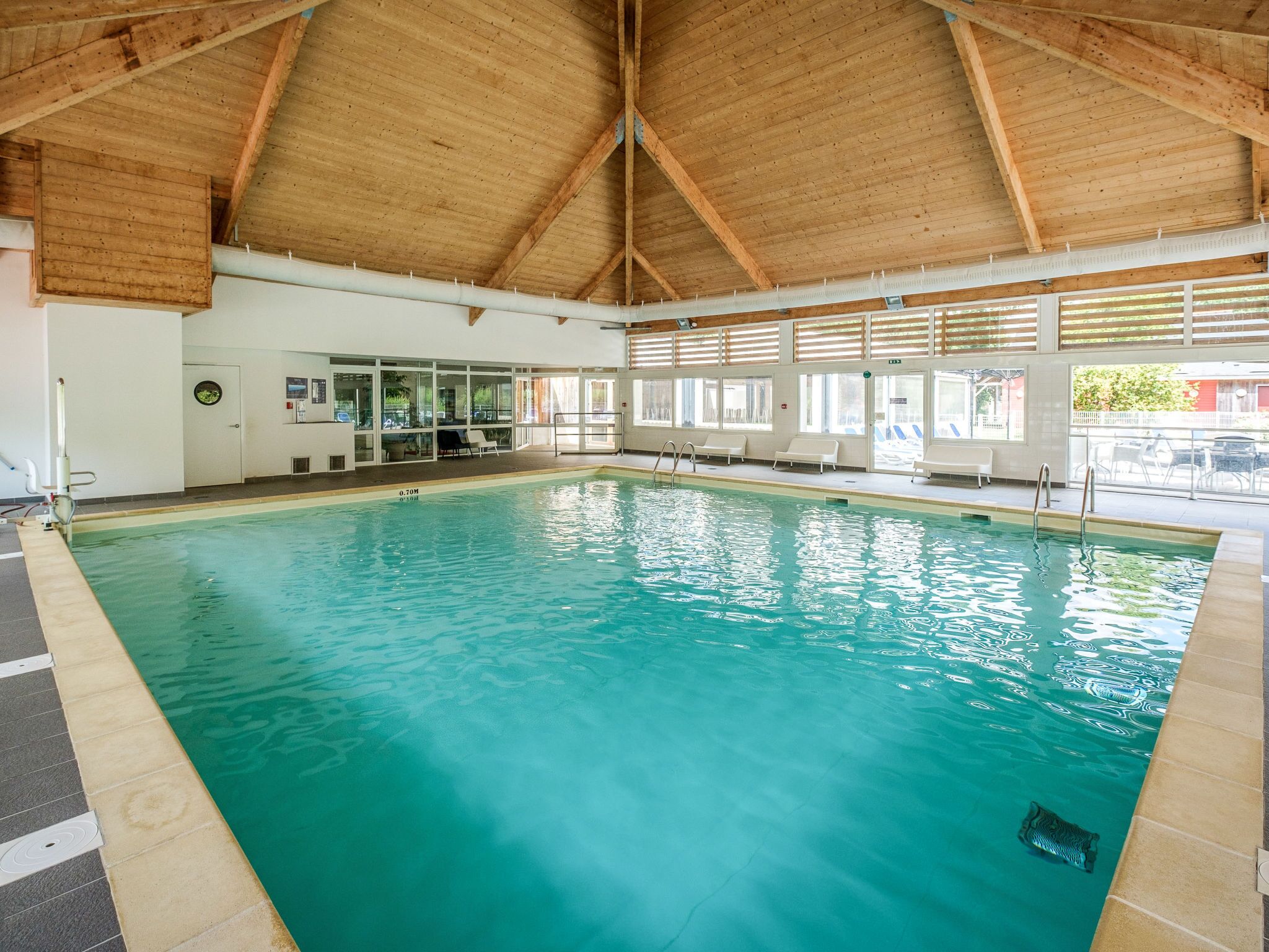An indoor swimming pool with clear water, wooden ceiling beams, and a tiled floor.