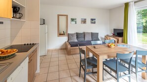 Eine moderne Küche mit Herd, Spüle und Schränken. Es gibt einen Essbereich mit Tisch und Stühlen, und ein Sofa im Hintergrund.