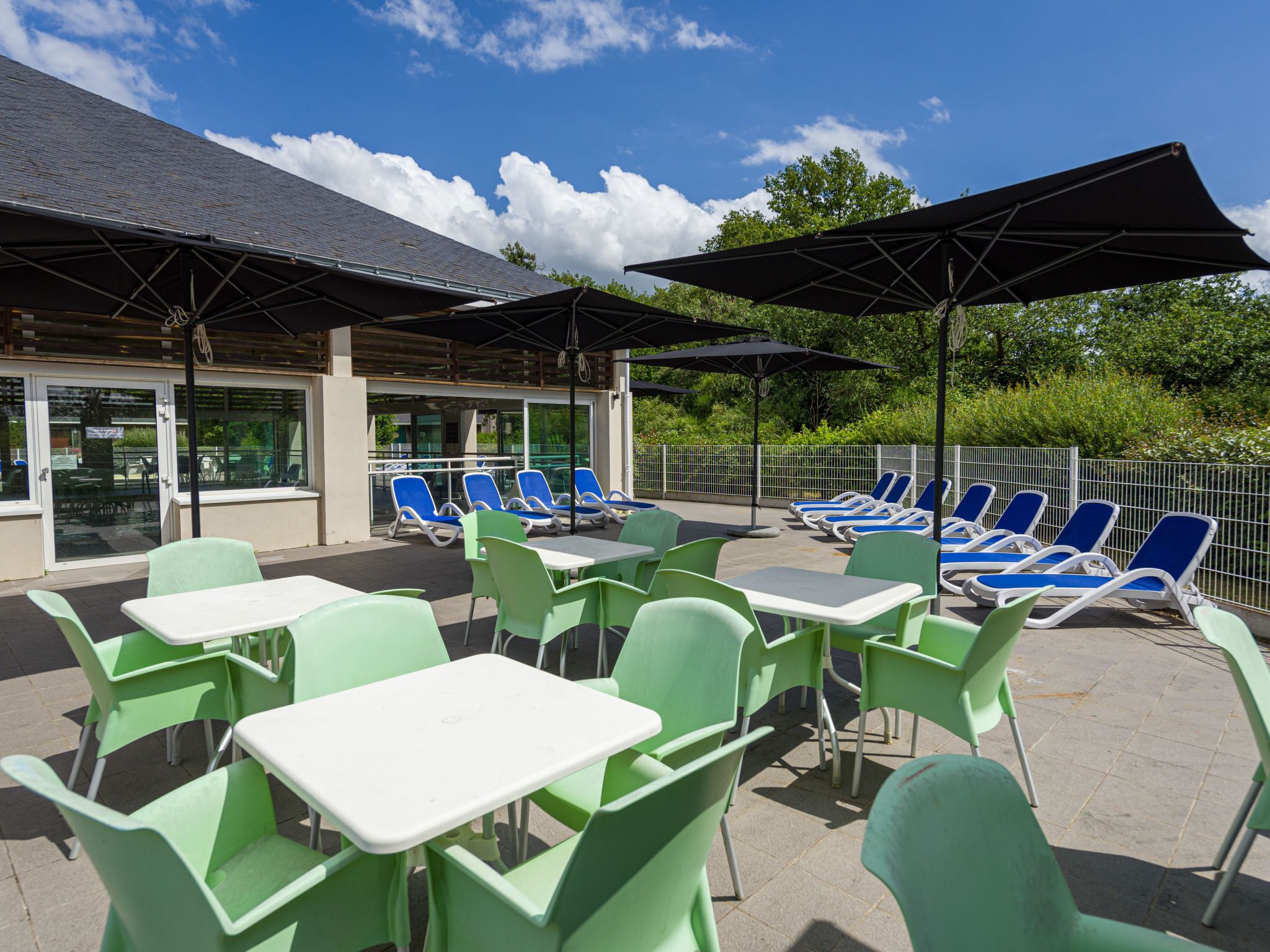 An outdoor patio area with green chairs and tables, sun loungers, and umbrellas.