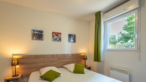 Ein Hotelzimmer mit einem großen Bett, zwei Nachttischen mit Lampen, einem Fenster mit Vorhängen und drei Wandbildern.