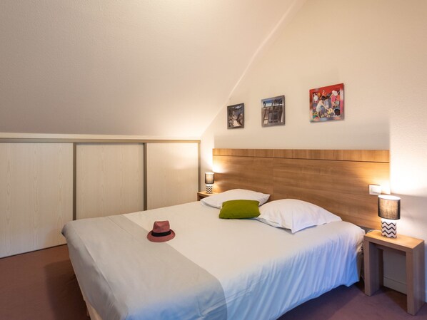 A bedroom with a large bed, wooden headboard, two bedside tables with lamps, and three framed pictures on the wall.
