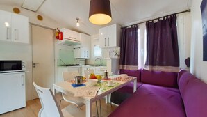 Cocina compacta con armarios blancos, microondas y comedor con mesa y sillas. Un sofá morado se encuentra en la sala.