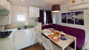 Cocina compacta con comedor, armarios blancos, estufa y una mesa dispuesta con frutas y un libro.