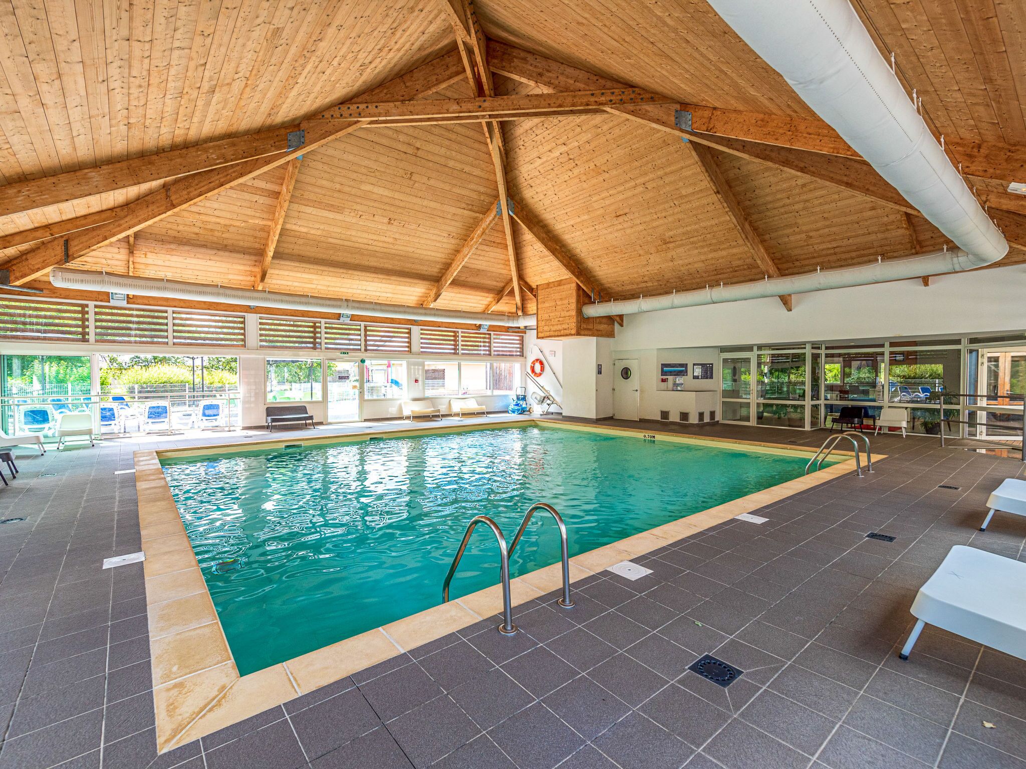 An indoor swimming pool with a wooden ceiling, clear glass windows, and a lifeguard chair.