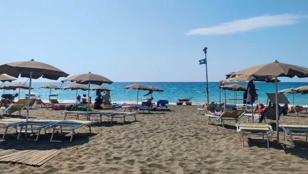 A beach with rows of sun loungers and umbrellas, a clear blue sky, and the ocean in the background. - Campeggio del Forte by Interhome (Marina di Bibbona)