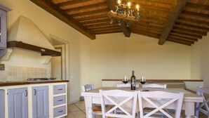 A kitchen with a dining area, wooden ceiling beams, and a chandelier. - Il Felciaione by Interhome (Riparbella)