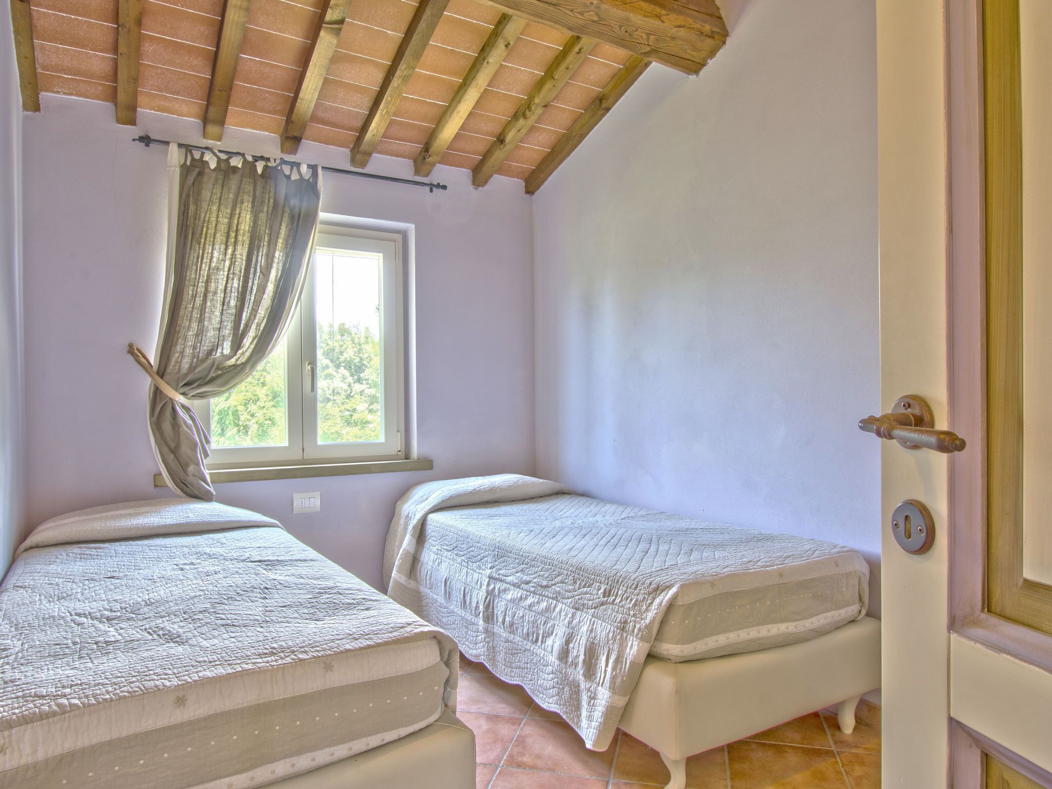 Une chambre avec deux lits simples, une fenêtre avec des rideaux, un plafond en bois et une porte.