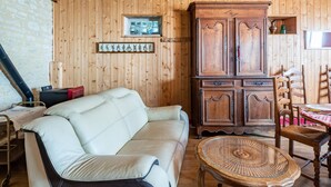Habitació acollidora amb parets de fusta, un sofà de pell blanca, un armari de fusta i una taula de centre de vimet.