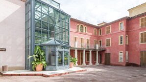 Une cour intérieure avec une véranda en verre, des plantes en pot et un bâtiment rouge doté de balcons.