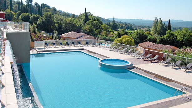 Une piscine rectangulaire avec un petit jacuzzi rond, entourée de chaises longues et d’une terrasse carrelée.