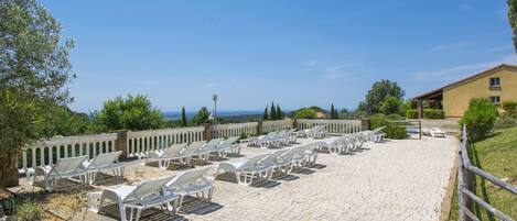 A paved outdoor area with rows of white sun loungers and a building in the background.