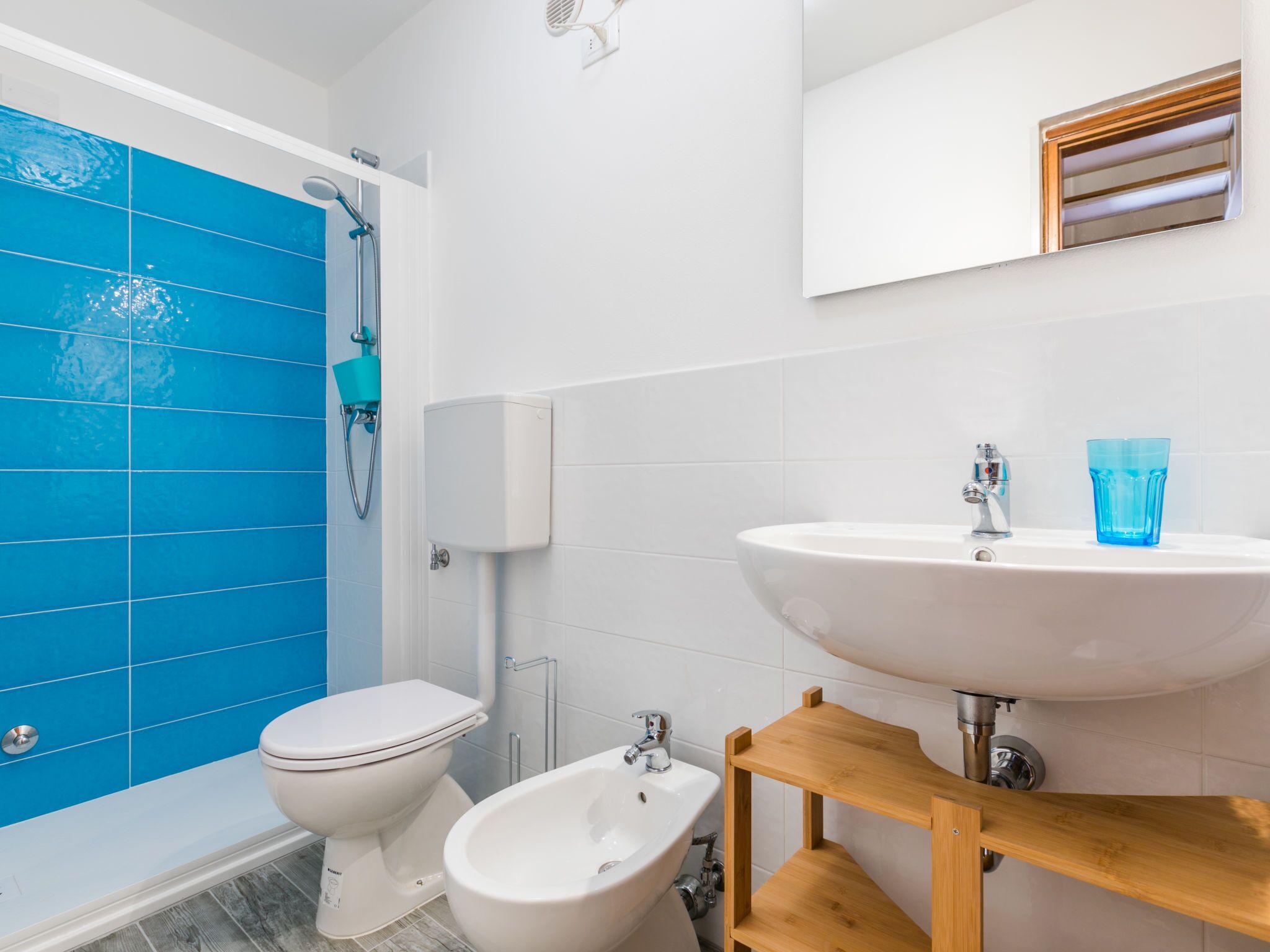 A bathroom with a white sink, a bidet, a toilet, and a shower with blue tiles.