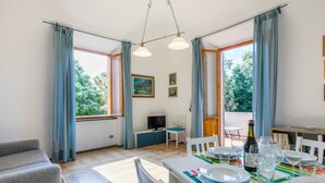 Uma área de refeições com uma mesa posta para dois, uma televisão e uma janela com cortinas.