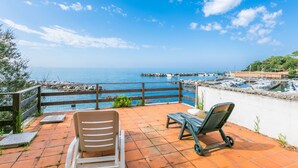 Terraço com duas cadeiras de descanso com vista para uma marina e o mar.
