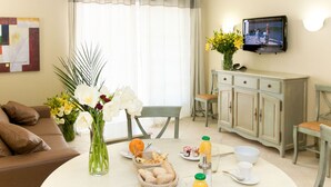Zona pranzo con tavolo rotondo apparecchiato per la colazione, un divano, un armadio e una TV a parete.