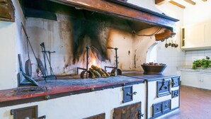 A rustic kitchen with a wood-burning stove, a large bowl of fruits, and a hanging pot rack. - Fattoria di Scaletta by Interhome (San Miniato)