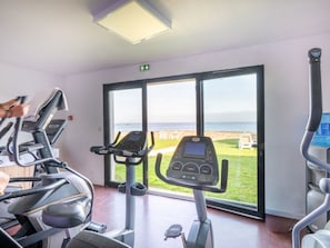 A gym with treadmills, a stationary bike, and a large window with a view of the beach. - Odalys Domaine des Roches Jaunes by Interhome (Plougasnou)