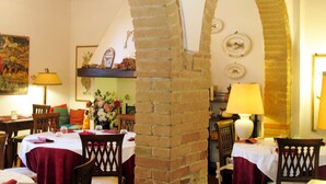 Ein Essbereich mit Backsteinbögen, Holztischen und -stühlen. Auf den Tischen stehen florale Tischdekorationen.