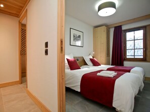 Two beds with crisp bedding, a wardrobe, and a framed picture adorn this stylish room with a view of the surrounding trees.