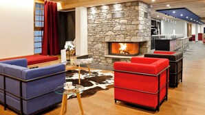 Un salon moderne doté d’une cheminée en pierre, de sièges rouges et bleus, et d’un plafond en bois.