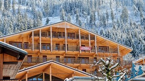 Un chalet en bois doté de plusieurs balcons, entouré d’arbres couverts de neige.