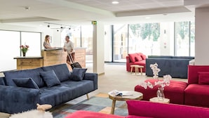 A modern hotel lobby with a reception desk, plush seating areas, and large windows offering views of the outdoors.