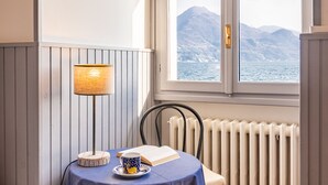 Habitació amb una taula posta per a dues persones, una làmpada i vista a una muntanya i al mar per una finestra.