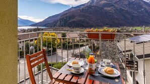 Un balcon avec une table préparée pour le petit-déjeuner, offrant une vue sur un paysage montagneux avec un lac.