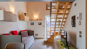 Un salon moderne avec un escalier en bois, un canapé agrémenté de coussins rouges et un coin repas avec une table en bois.