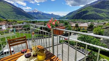 Un balcone con un tavolo apparecchiato per due, con vista su un pittoresco paesaggio montuoso e un lago.