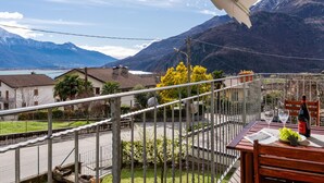 Un balcon avec une table dressée pour deux personnes, offrant une vue sur un paysage montagneux et un plan d’eau.