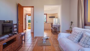 A living room with a TV, wooden furniture, a sofa, and a dining area with a kitchen in the background. - Finca Can Corritx by Interhome (Muro)