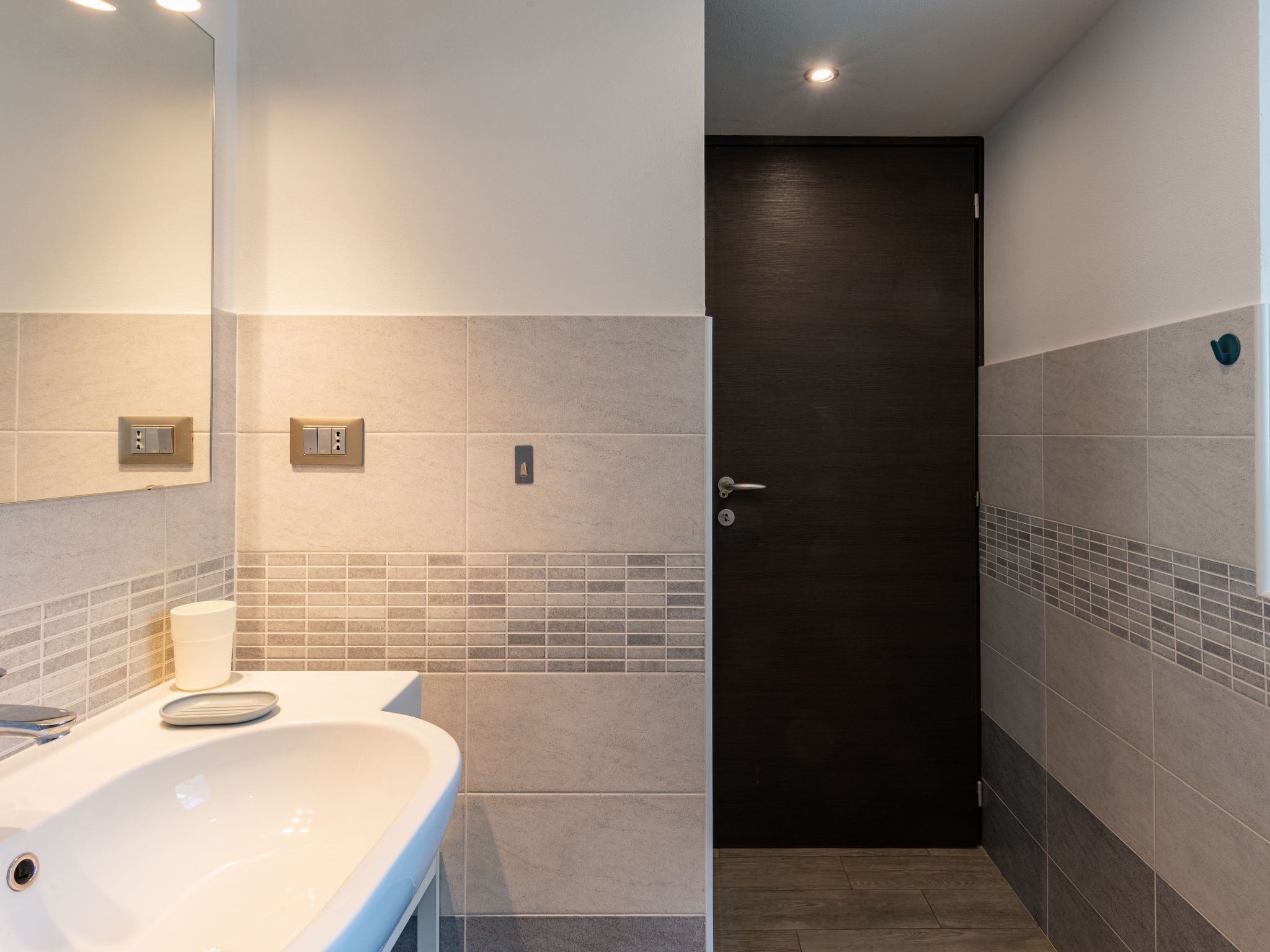 A modern bathroom with a white sink, mirror, and tiled walls.