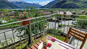 A balcony with a table, two chairs, a potted plant, and a view of mountains and a lake. - Apartment Marco by Interhome (Lago di Mezzola)