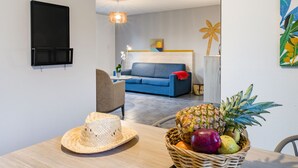 A modern living room with a blue sofa, a dining table with a wicker basket of fruit, and a wall-mounted TV. - Domaine du Golf by Interhome (Montpellier)