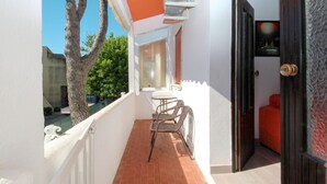 Ein schmaler Balkon mit Fliesenboden, einem kleinen Tisch mit Stühlen und einer Tür zu einem Zimmer mit einem Bett.