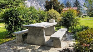 A stone picnic table with benches in a garden with mountains in the background.