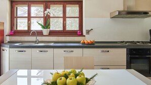 A modern kitchen with a large window, a sink, a stove, and a bowl of apples on the counter.