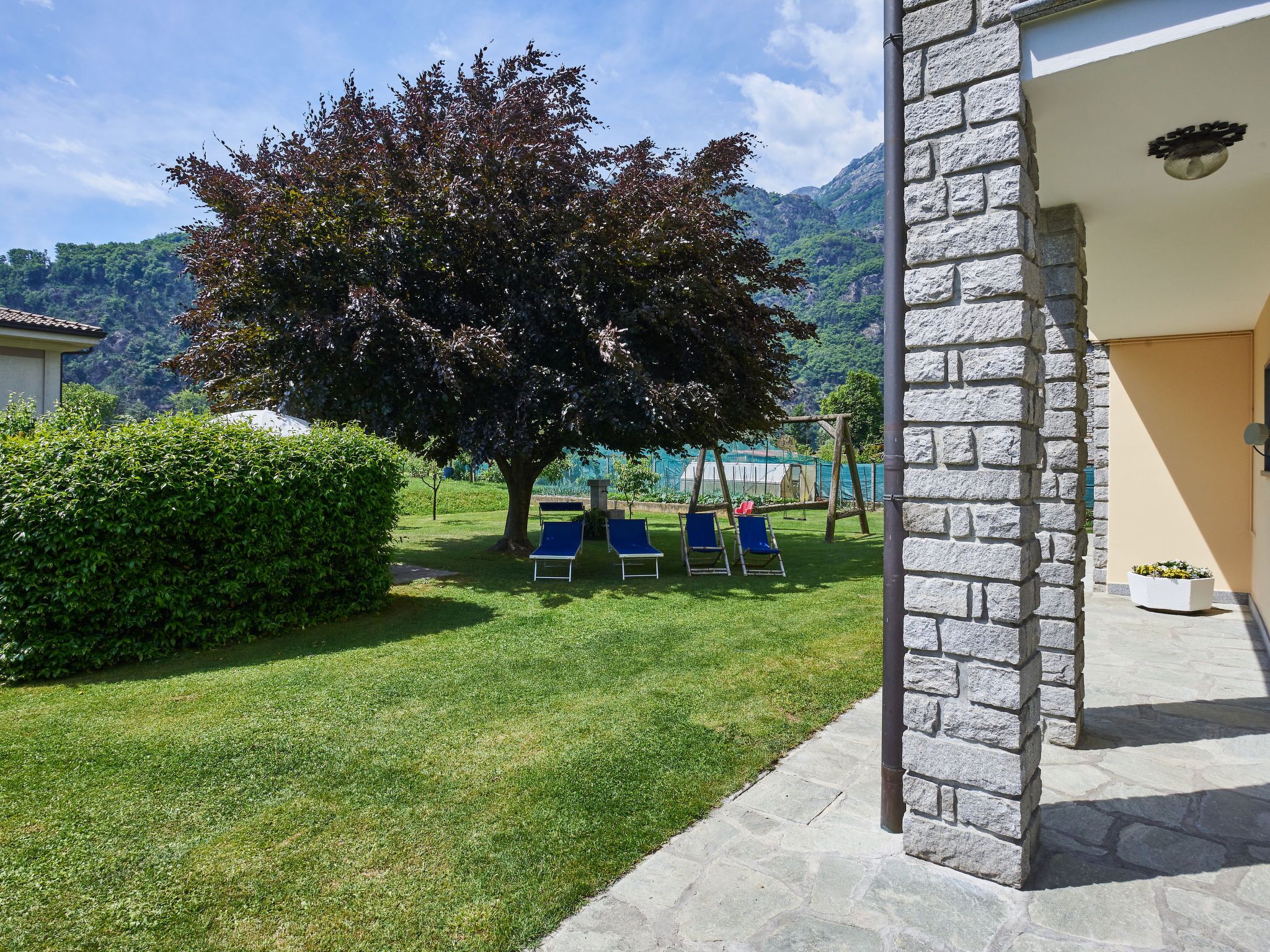 Un edificio in pietra con un prato, un albero grande e poltrone da relax blu.