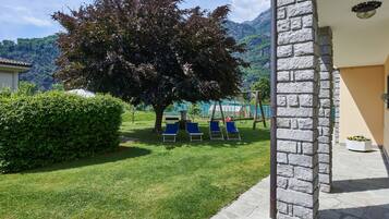Un edificio in pietra con un prato, un albero grande e poltrone da relax blu.