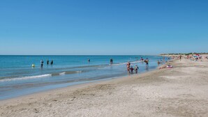 Ein Strand mit Menschen, die am Ufer entlanggehen, einige im Wasser, und Strandbesucher, die in der Sonne entspannen.