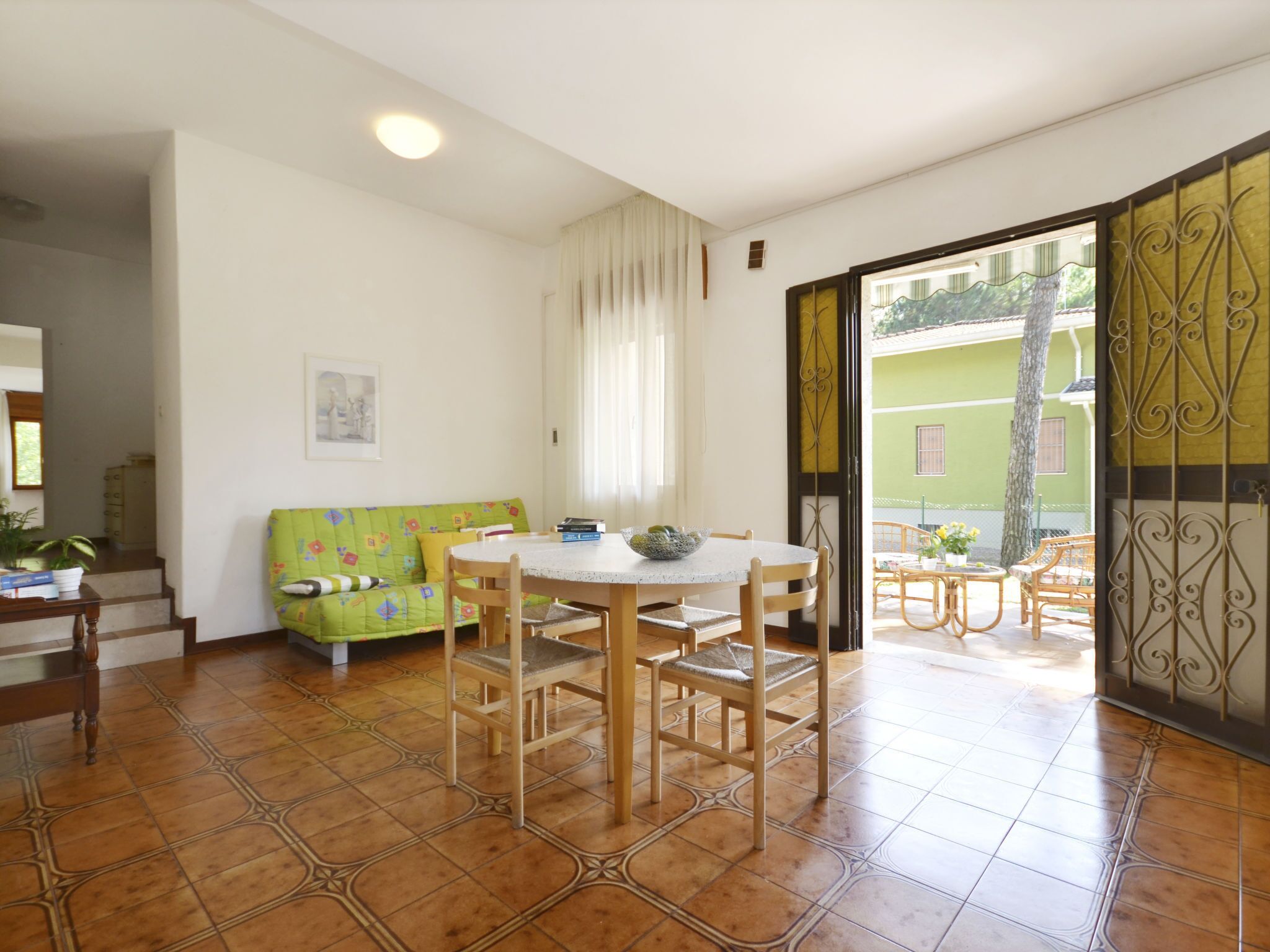 Ein Essbereich mit rundem Tisch und Stühlen, einer grünen Couch und einem Fenster mit Vorhängen.