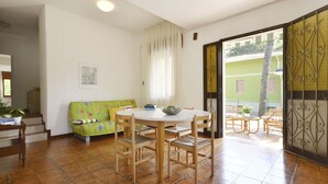 A dining area with a round table and chairs, a green sofa, and a window with curtains. - Missana by Interhome (Lignano Riviera)
