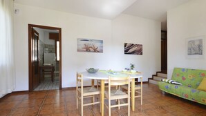 A dining area with a round table and chairs, a green sofa, and a staircase leading to another level. - Missana by Interhome (Lignano Riviera)