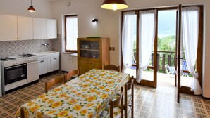 Cuina amb taula de menjador, cadires i vista a una zona exterior amb balcó per la porta oberta.