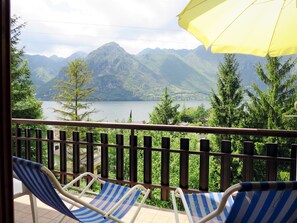 A balcony with two striped lounge chairs and a yellow umbrella, overlooking a lake and mountains. - Villa Martinelli by Interhome (Lago d'Idro)