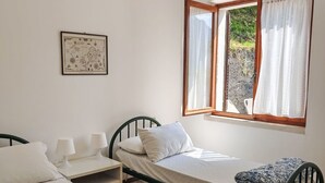 Un llit individual amb matalàs blanc i manta estampada, una taula de nit amb làmpada, un mapa emmarcat a la paret i una finestra amb cortines.