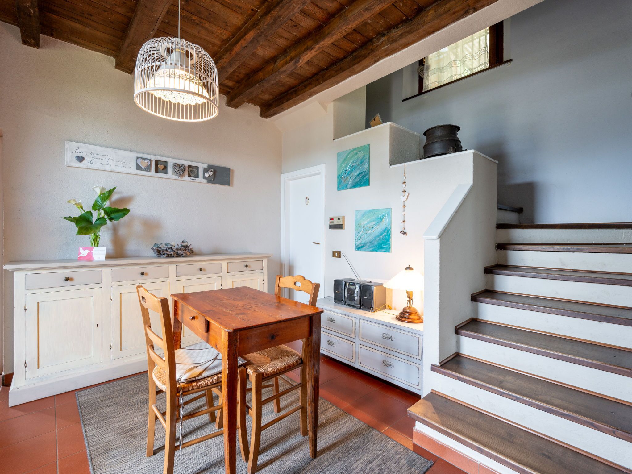 Een keuken met een houten tafel en stoelen, een wit kastje en een trap.