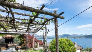 Een tuin met een pergola, buitenmeubels en uitzicht op een meer en bergen.