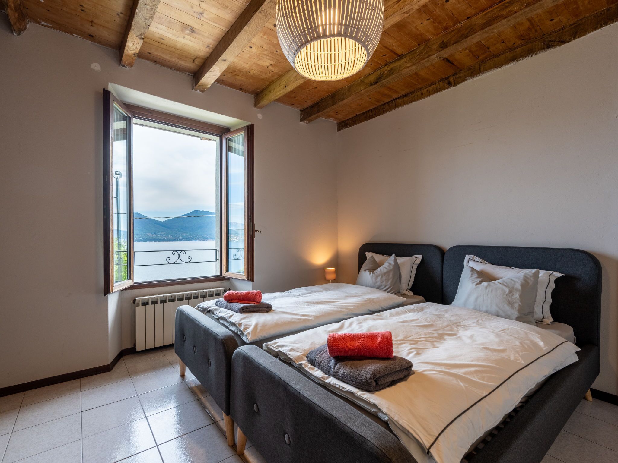 A bedroom with two beds, a large window with a view of mountains, and a wooden ceiling.